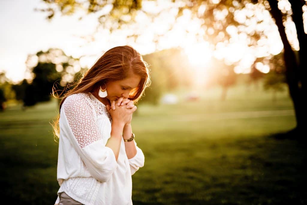 woman in white shirt praying outside at golden hour