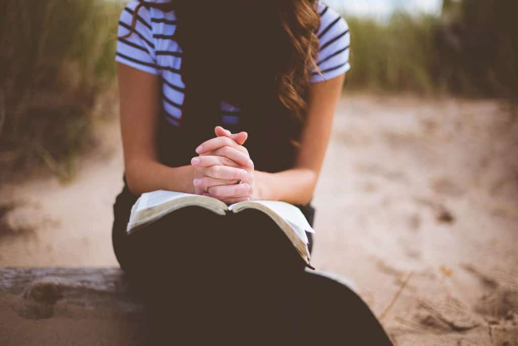 woman praying with hands folded over open bible - no face shown