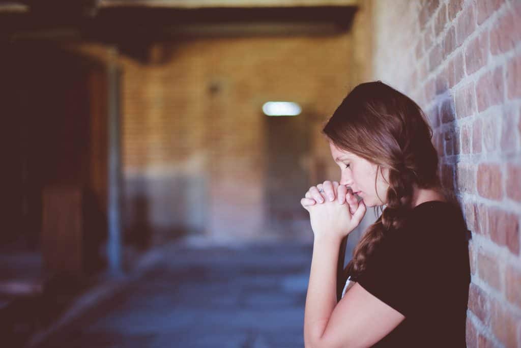 woman in dark shirt and braided hair praying in hallway